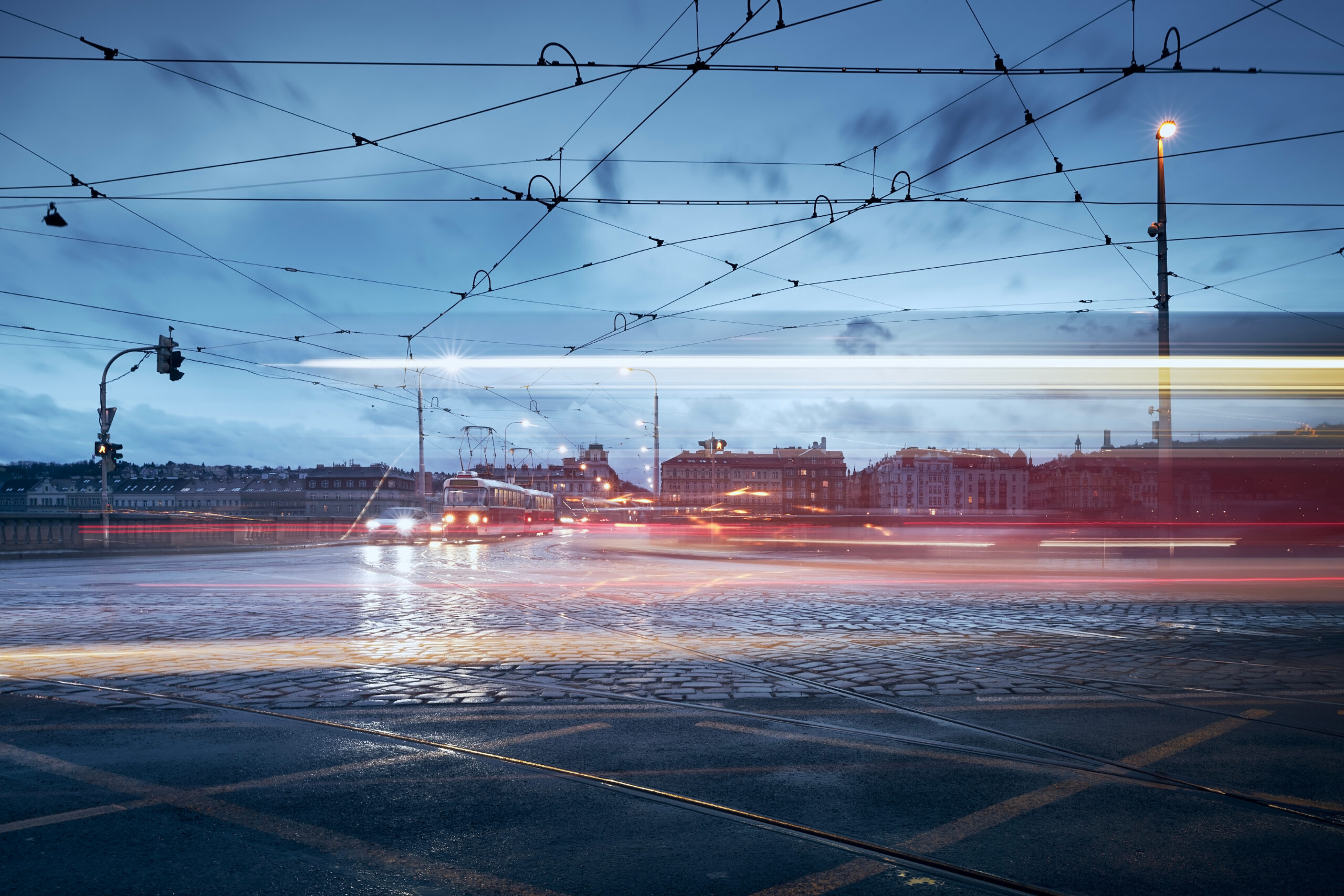 Light trails of tram in Prague downtown. Busy road intersection in city at rainy evening.